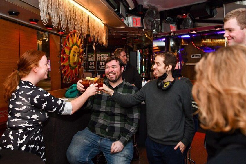 A group of people in a bar with a mural and a sign that reads 'ENTER HERE.' 3