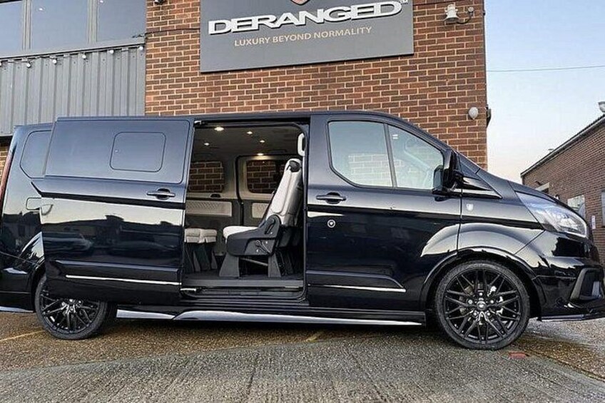 Een zwarte bus geparkeerd voor een gebouw met een bord waarop staat 'DERANGED LUXURY BEYOND NORMALITY'. 2