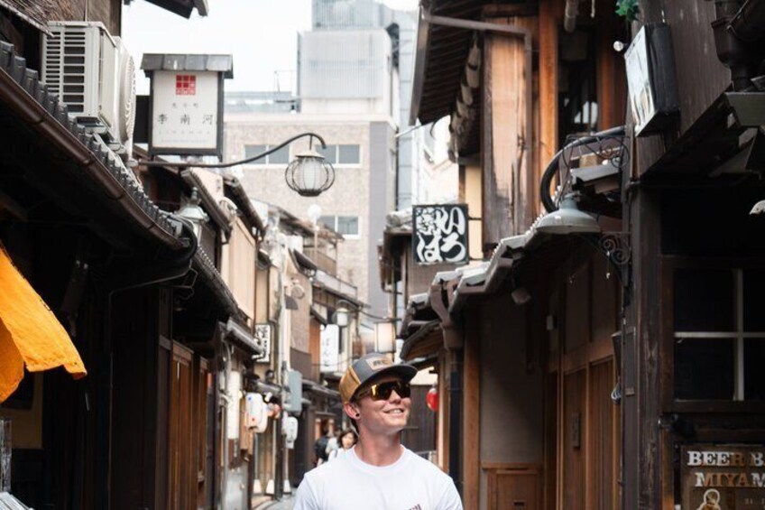 Una calle estrecha con edificios tradicionales de madera, una persona caminando y un letrero con caracteres japoneses. 4