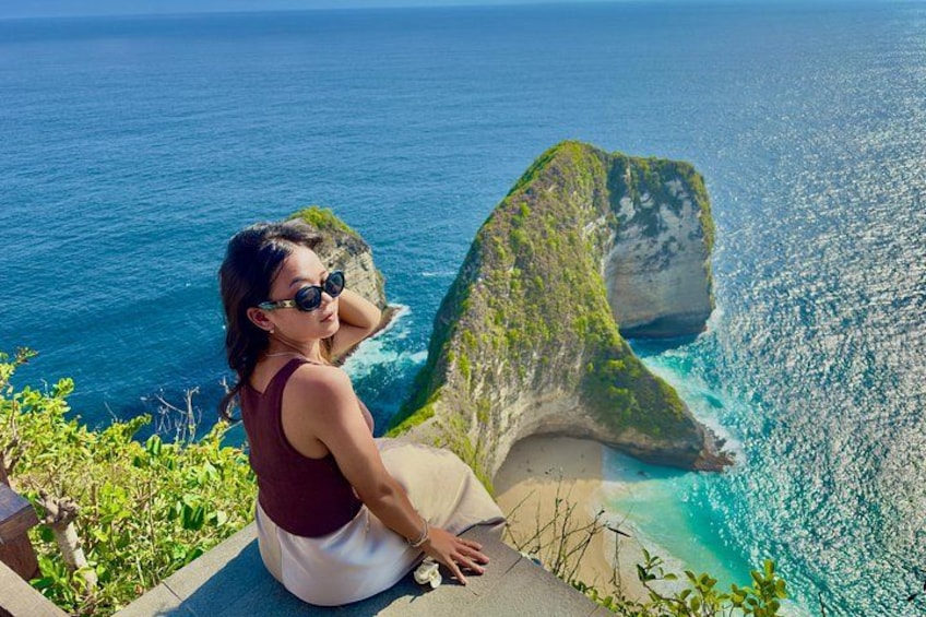 A person sitting on a ledge overlooking a coastal cliff with a view of the ocean. 1