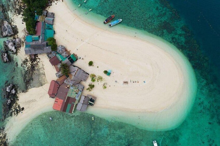 Une vue aérienne d’une plage aux eaux turquoise et limpides, bordée d’un rivage sablonneux, et où se trouve un petit village avec des bâtiments aux couleurs vives. 3