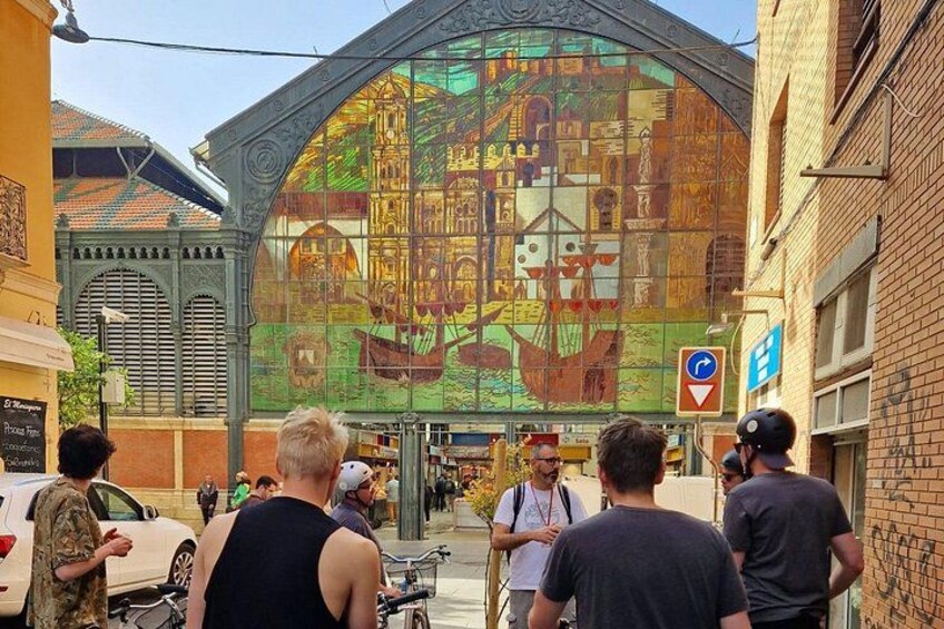 A colorful mosaic mural on a building, a street with pedestrians, and a blue directional sign. 3