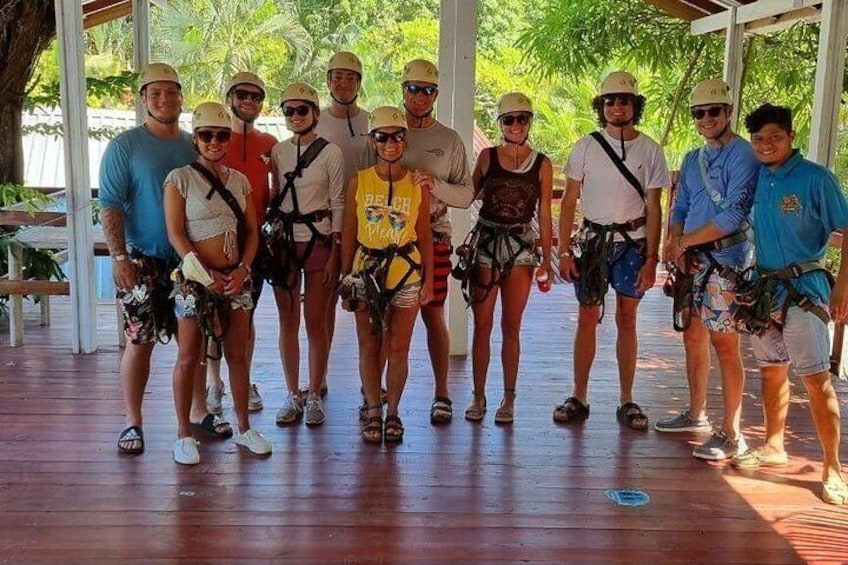 A group of people in a covered area with a wooden floor, wearing helmets and harnesses, suggesting a safety activity. 3