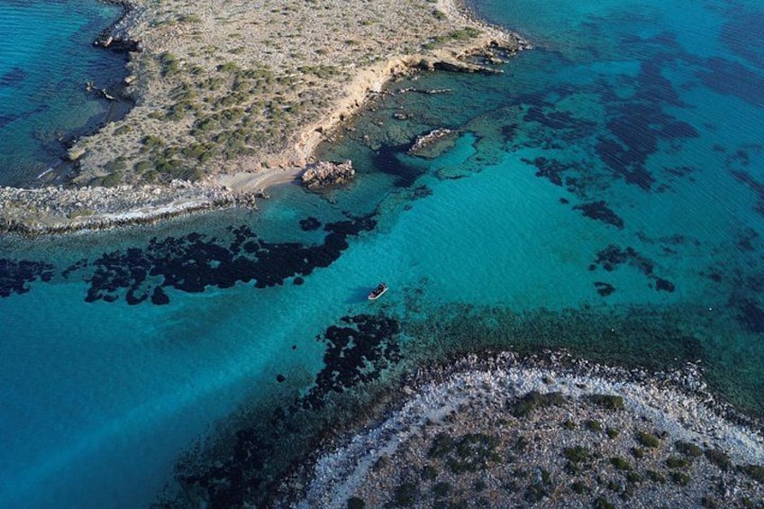 An aerial view of a coastal area with clear blue waters, rocky terrain, and sparse vegetation. 1