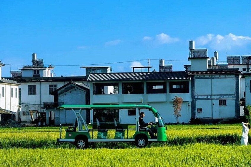 A green vehicle in a field with buildings in the background. 4
