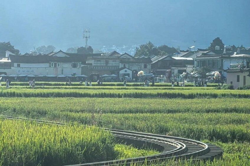 A rural landscape with a curved railway track, green fields, and traditional buildings in the background. 2