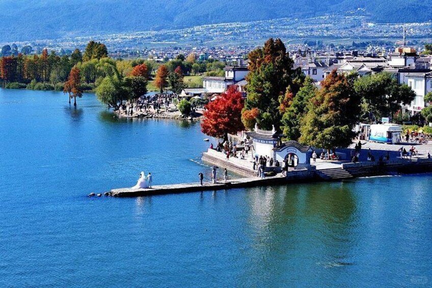 A lake with a pier, trees, and a town in the background. 3