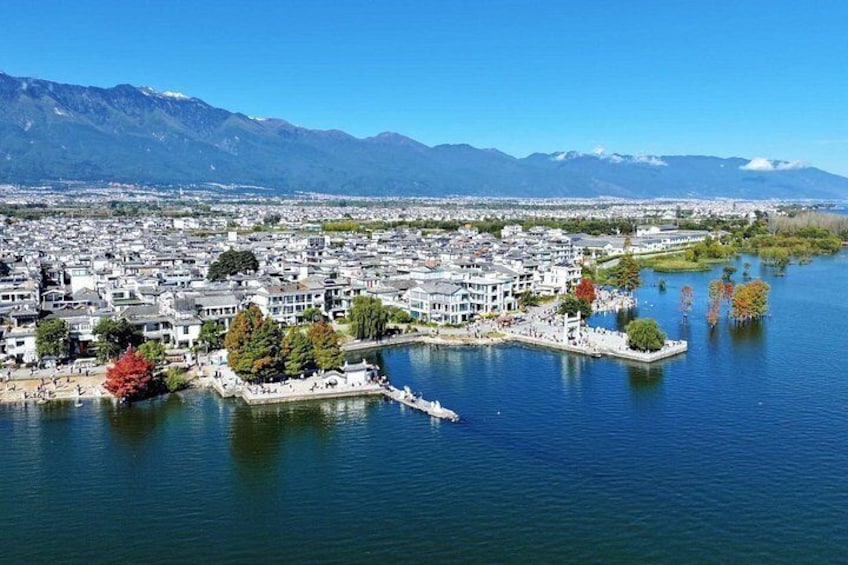 A lakeside town with traditional buildings, a dock, and mountains in the background. 2
