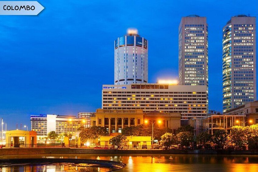 A cityscape with illuminated buildings, a reflective water body, and a clear sky. 2