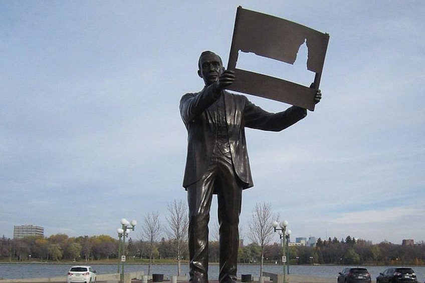 A statue of a man holding a sign, with a body of water and trees in the background. 1