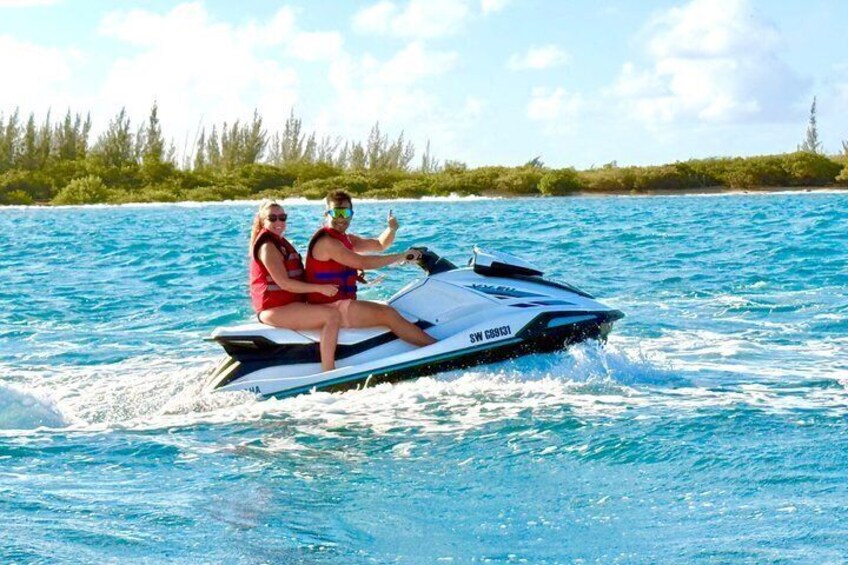 Two people jet-skiing on a body of water with a forested shoreline in the background. 1