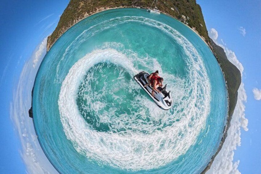 A person riding a jet ski on a large, circular wave in turquoise water. 3