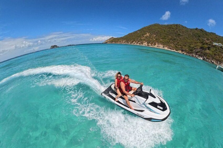 Two people jet-skiing on turquoise water with a mountainous island in the background. 4