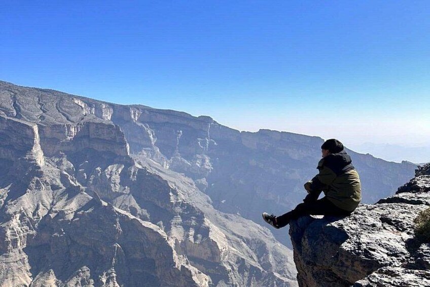 A person sitting on a rock overlooking a canyon with layered rock formations. 3