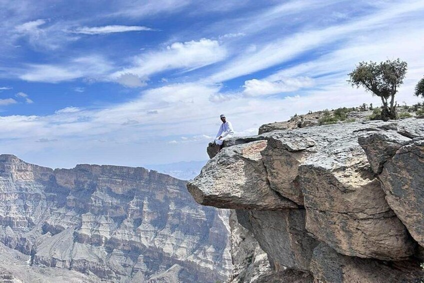 A person sitting on a rock ledge overlooking a canyon with layered rock formations. 2