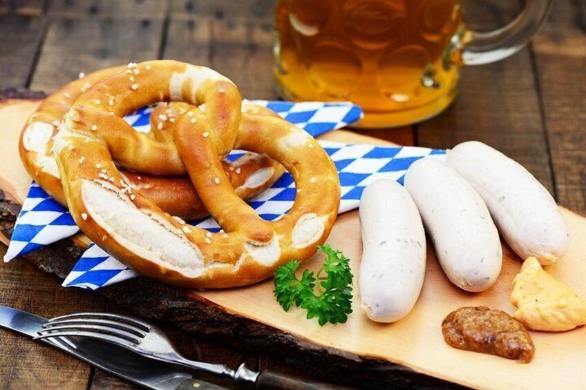 A pretzel, sausages, a beer mug, and a fork on a wooden table. 5