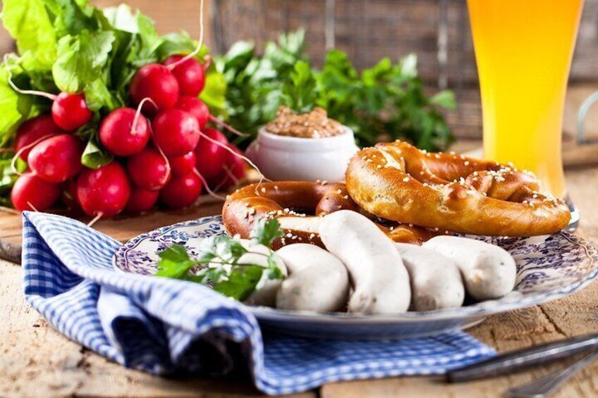 A plate with pretzels, sausages, and radishes, a glass of orange juice, and a checkered cloth. 2