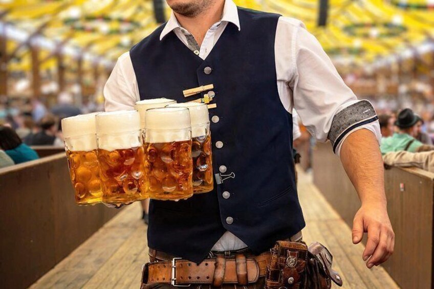 A man in traditional attire holding multiple beer mugs. 3