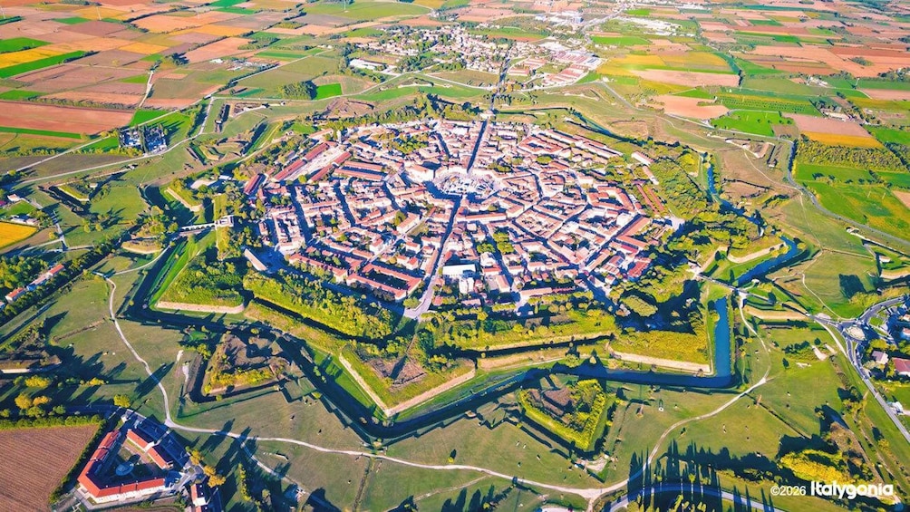 An aerial view of a circular fortified town with surrounding fields and a river. 1