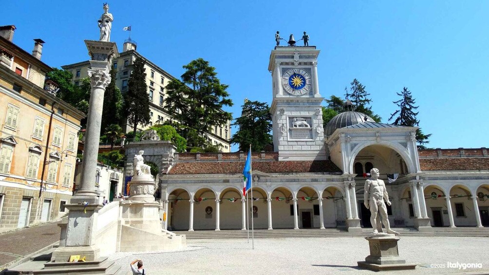 A plaza with a clock tower, statues, and a fountain. 3