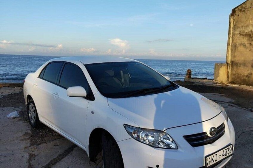 Een witte auto geparkeerd in de buurt van de kust, met een heldere lucht en een verre horizon van de zee. 2