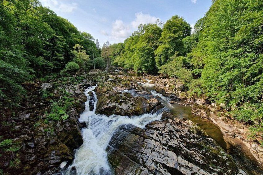 A waterfall in a forested area with dense greenery and rocky terrain. 2