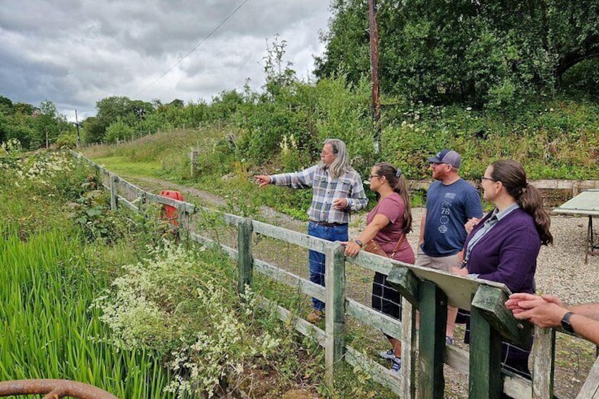 A group of people standing by a wooden fence in a natural setting with greenery and a cloudy sky. 4