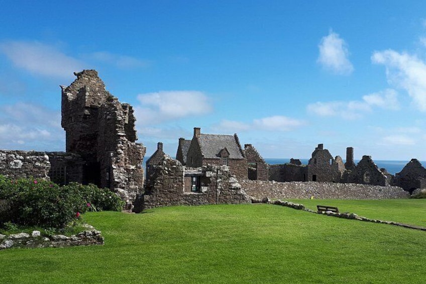 A historic stone building with ruins, a grassy lawn, and a clear blue sky. 1