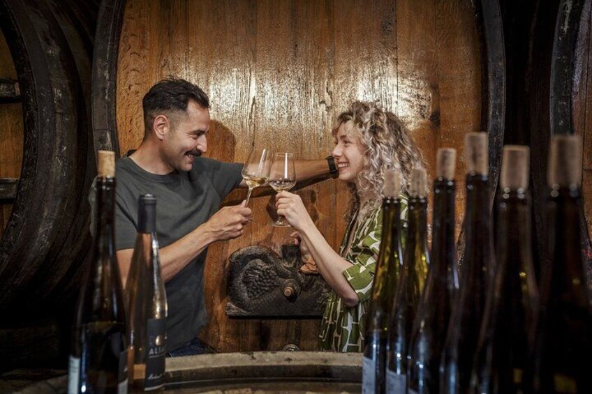 Two people toasting with wine glasses in a cellar with wooden barrels and bottles. 1
