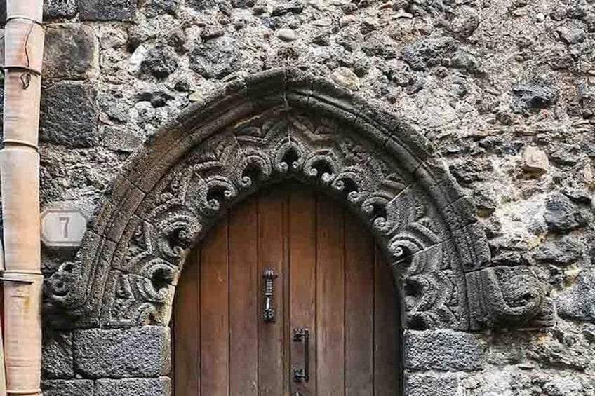 A stone building with a wooden door, a stone archway, and a number '7' sign. 3