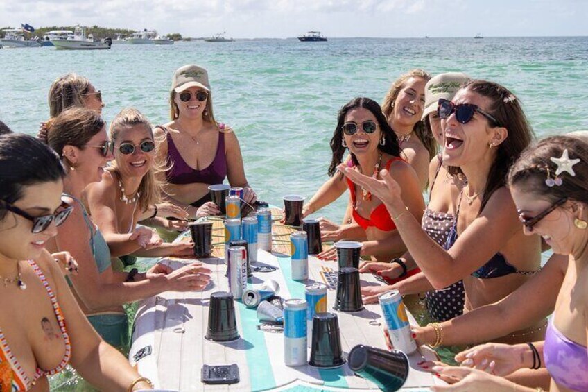 Un grupo de personas sentadas en una mesa en un barco, con el océano y otros barcos al fondo. 2