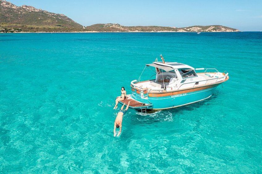A boat with two people on a turquoise sea, a dock, and distant hills. 2