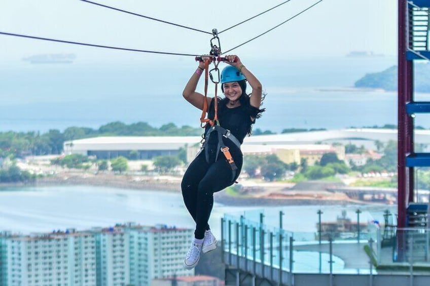 En person åker på en zipline över ett vattenområde med byggnader i bakgrunden. 2