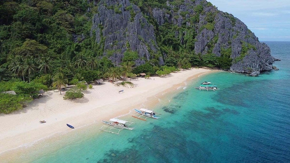 A tropical beach with clear turquoise waters, a sandy shore, and a rocky cliff. 2