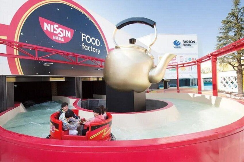 Een waterattractie met een grote theepotstructuur, omgeven door een rode en zwarte thematiek met logo's van Nissan en Fashion Factory. 2