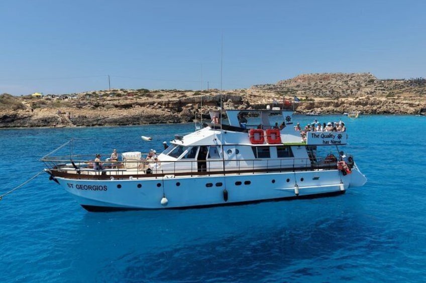 Un barco blanco llamado ST GEORGIOS sobre aguas azules cristalinas, con terreno rocoso al fondo. 5