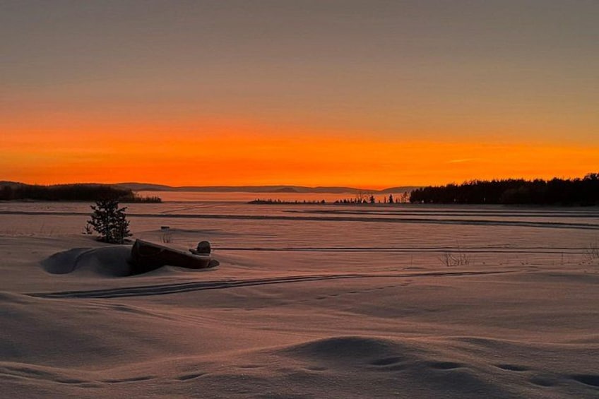 A snowy landscape at sunset with a tree and a snow-covered object. 3