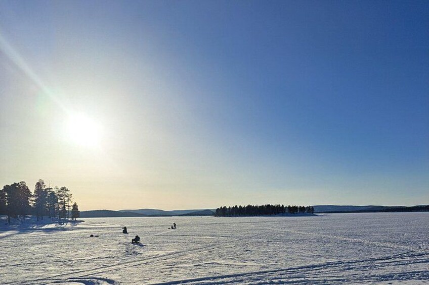 A snowy landscape with a clear sky, a distant tree line, and a few people in the distance. 5