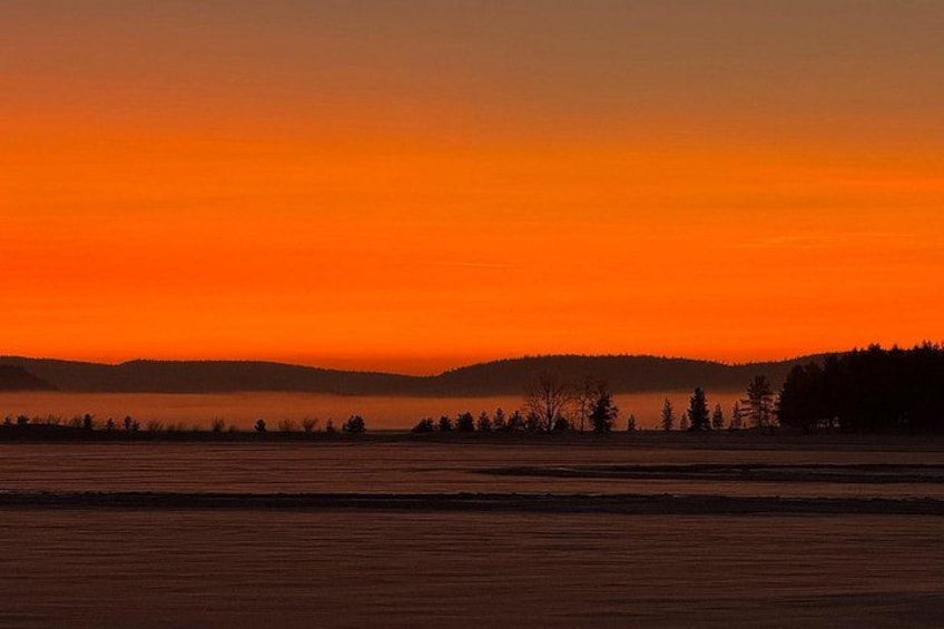 A sunset over a flat landscape with distant hills and a line of trees. 4