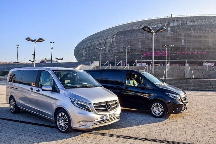 Two parked cars in front of a large stadium. 4
