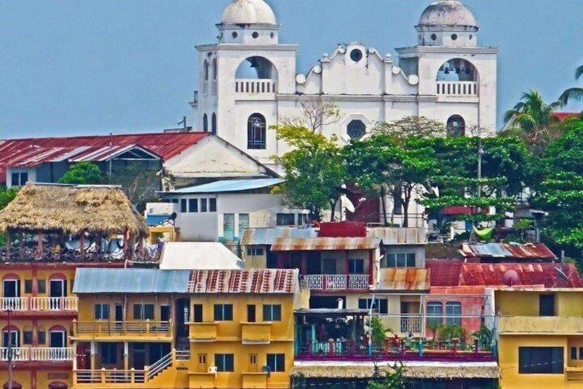 A colonial church with two domes, colorful buildings, and a thatched-roof structure. 2