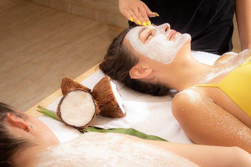 A person receiving a facial treatment with coconut shells and a yellow garment. 1