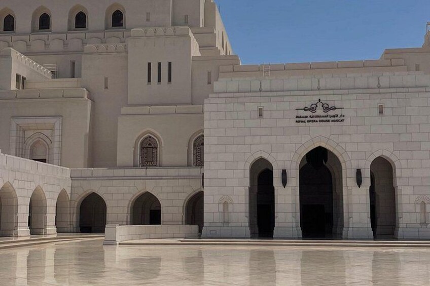 A large, white building with arched doorways and a sign that reads 'Royal Opera House Muscat.' 3