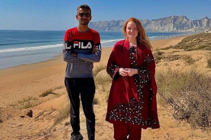 Two people standing on a beach with a cliff and ocean in the background. 3