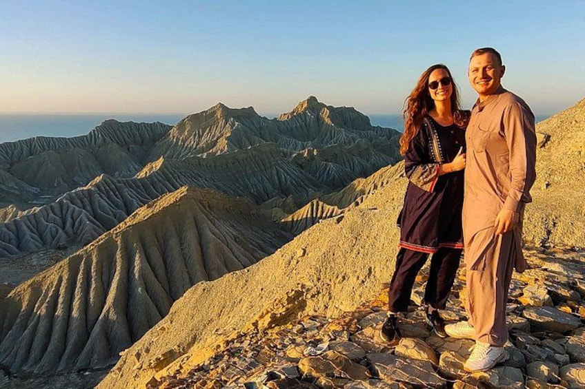 A couple standing on a rocky mountain peak with a panoramic view of rugged terrain and distant mountains. 1