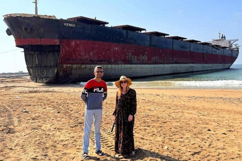 A beach with a large shipwreck and two people standing in the foreground. 4