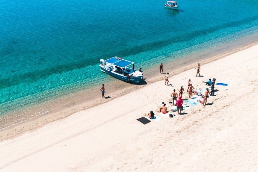 A beach with people sunbathing and swimming, a boat, and clear turquoise water. 1