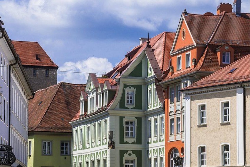 A row of colorful historic buildings with red-tiled roofs and traditional European architecture. 1