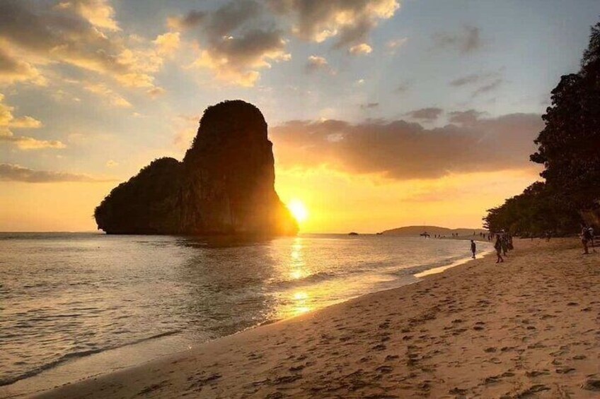 Una spiaggia al tramonto con una grande formazione rocciosa e persone che passeggiano sulla riva. 5