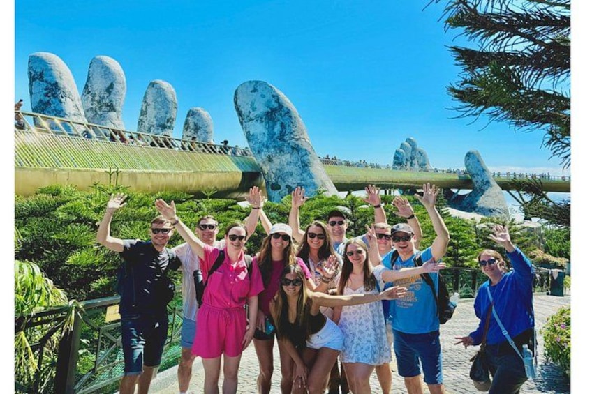 A group of people posing in front of a large rock formation with a bridge in the background. 1